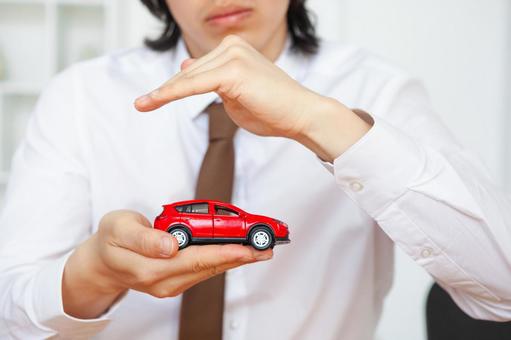 手のひらの赤い車の模型を守る男性スタッフの手元 包む,守る,保険業の写真素材