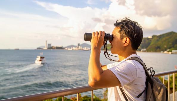 双眼鏡で海の先を見ている男性 双眼鏡で海の先を見ている男性の写真