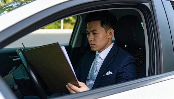 手もとに書類を持って運転するサラリーマン 手もとに書類を持って運転するサラリーマンの写真
