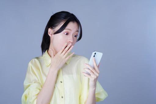 スマホを見て驚く黄色い服の女性 女性,スマートフォン,持つの写真素材