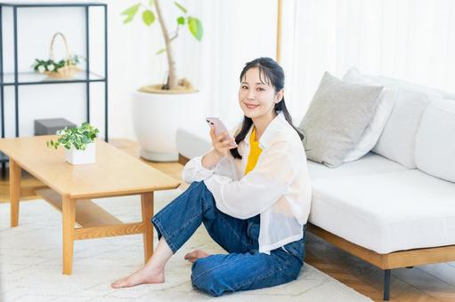 部屋でスマホを操作する女性 部屋でスマホを操作する女性 スマホ,笑顔,部屋の写真素材