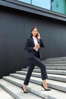 オフィスビルの外の階段でコーヒー片手に電話している女性 ビジネスウーマン,ビジネス,女性の写真素材