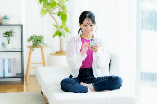 部屋でスマホを操作する若い女性 スマホ,笑顔,若い女性の写真素材