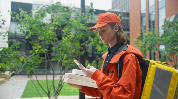 ピザ箱を持ってスマートフォンを使うフードデリバリーの男性 配達,フードデリバリー,デリバリーの写真素材