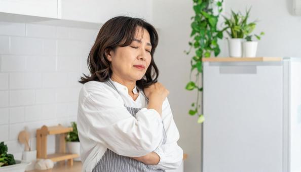 キッチンで肩こりを感じるエプロン姿の女性 キッチンで肩こりを感じるエプロン姿の女性の写真