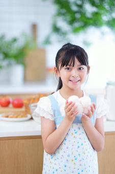野菜の並ぶキッチンで笑顔を見せる子ども 女の子,卵,持つの写真素材