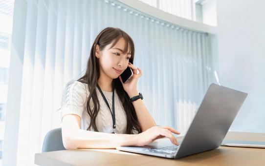 スマホで話しながらパソコンを使う女性 スマホで話しながらパソコンを使う女性 女性,パソコン,スマホの写真素材
