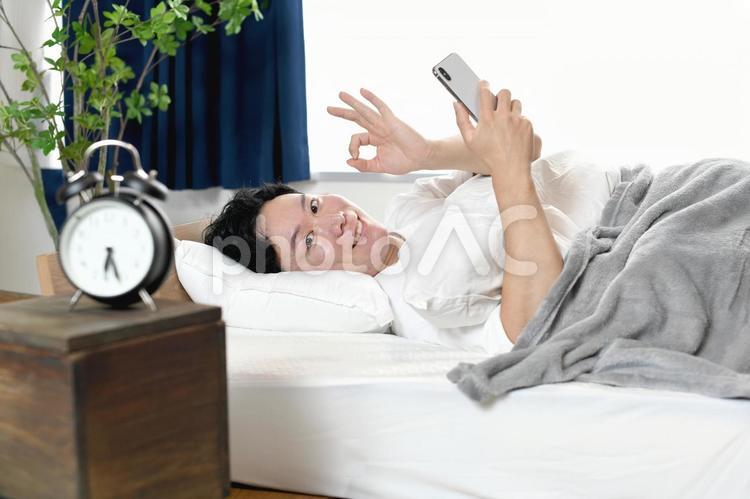 ベッドでスマホを持ちOKをする若い男性 男性,スマホ,ベッドの写真素材
