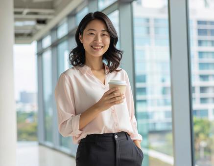 コーヒーを手に微笑む女性ビジネスパーソンの写真