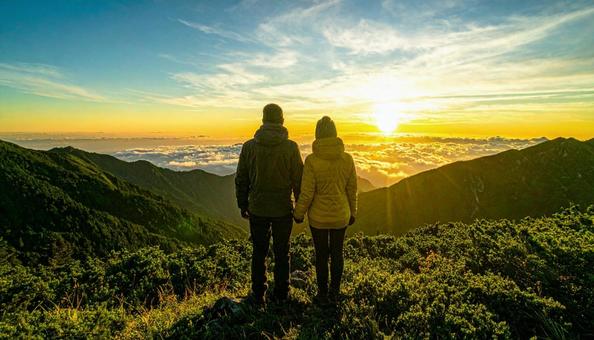 山から朝日を眺める日本人カップル 山から朝日を眺める日本人カップルの写真
