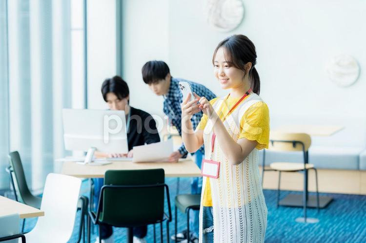 オフィスでスマホを操作する若い女性 スマホ,笑顔,女性の写真素材