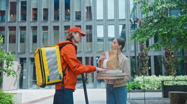 屋外でフードデリバリーを配達員から受け取る女性の写真