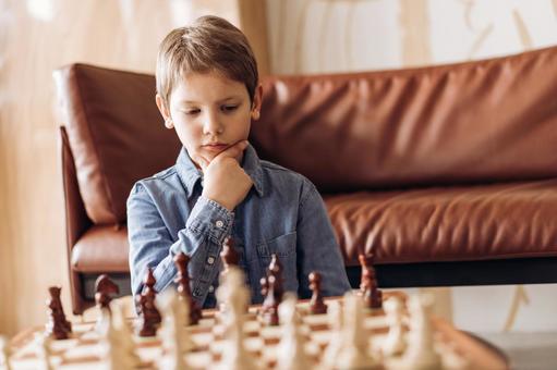 ソファテーブルで考えながらチェスをする男の子 ソファテーブルで考えながらチェスをする男の子の写真