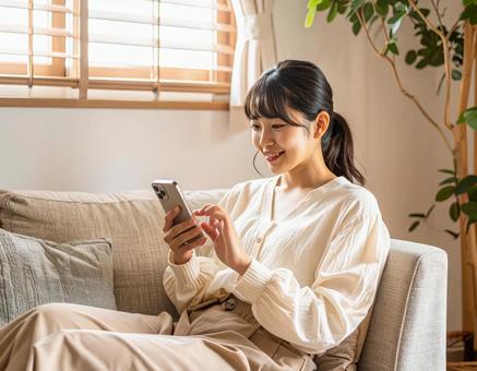 自宅のリビングでスマホを操作する女性の写真