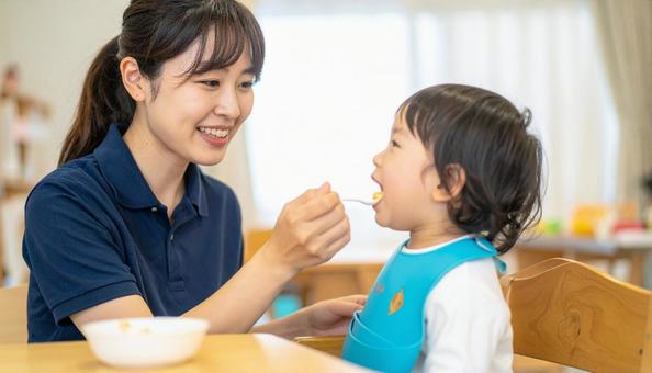 子どもにご飯をあげる保育士の写真