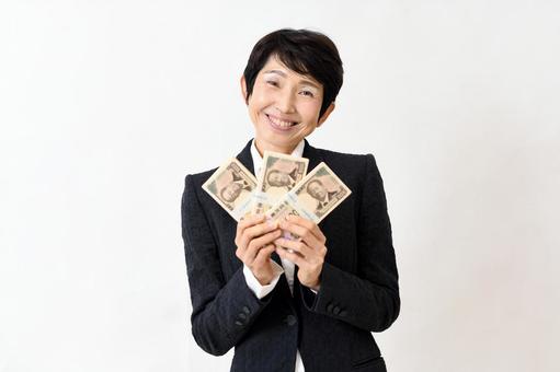 札束を持ち喜ぶスーツ姿の笑顔のミドル女性 ミドル女性,お金,札束の写真素材