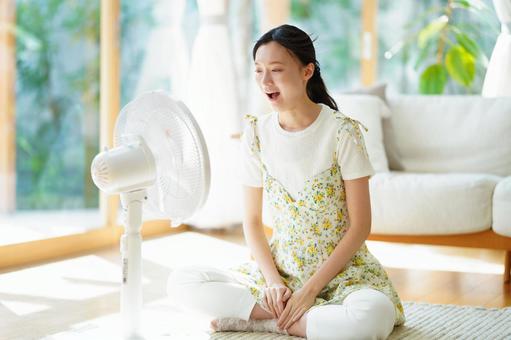扇風機に向かって声を出す女性の写真