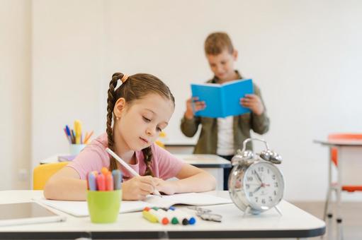 真剣に勉強する女の子と後ろでノートを読む男の子の写真