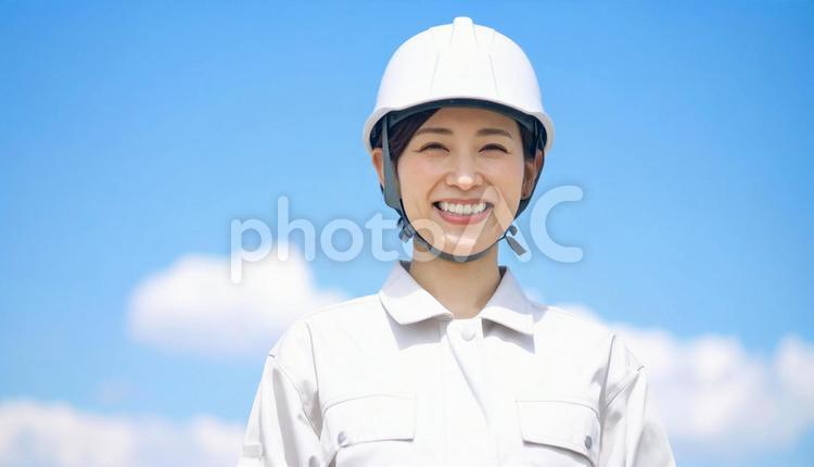 青空の下で笑顔の作業服を着た若い女性 人物,女性,作業服の写真素材