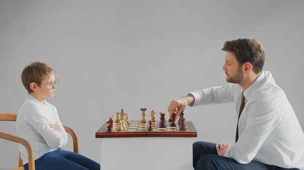 向かい合いチェスをする男の子とお父さん(グレー背景) 向かい合いチェスをする男の子とお父さん(グレー背景) チェス,親子,お父さんの写真素材