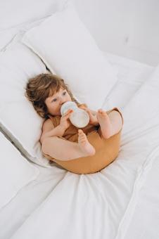 仰向けで足を上げてミルクを飲む子供 仰向けで足を上げてミルクを飲む子供 赤ちゃん,哺乳瓶,ミルクの写真素材