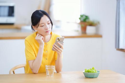 頬杖でスマホを見る黄色い服の女性の写真
