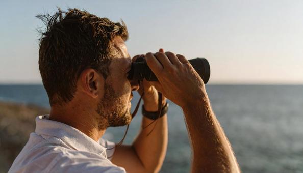 双眼鏡で海の先を見ている男性 双眼鏡で海の先を見ている男性の写真
