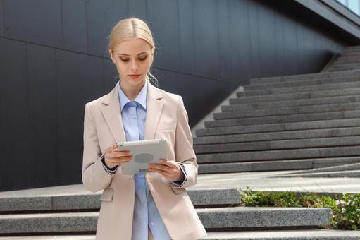 オフィスビルの外の階段でタブレットを見るビジネスウーマン ビジネスウーマン,ビジネス,女性の写真素材