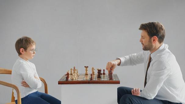 向かい合ってチェスをする男の子とお父さん(グレー背景) 向かい合ってチェスをする男の子とお父さん(グレー背景) チェス,親子,お父さんの写真素材