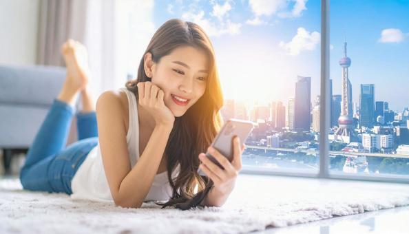 リビングで横になりスマホを操作する女性 リビングで横になりスマホを操作する女性の写真