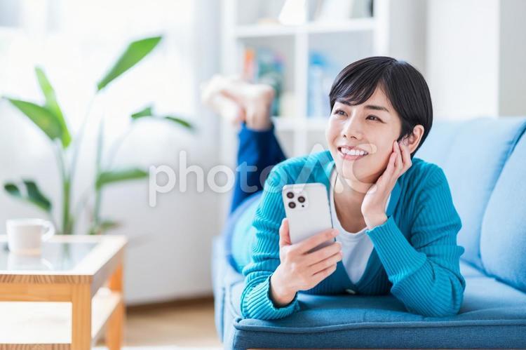 ソファーでスマホを操作する若い女性。 ソファー,メール,ショートヘアの写真素材