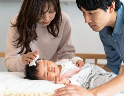 熱を出す赤ちゃんを心配そうに見守る夫婦 熱を出す赤ちゃんを心配そうに見守る夫婦の写真