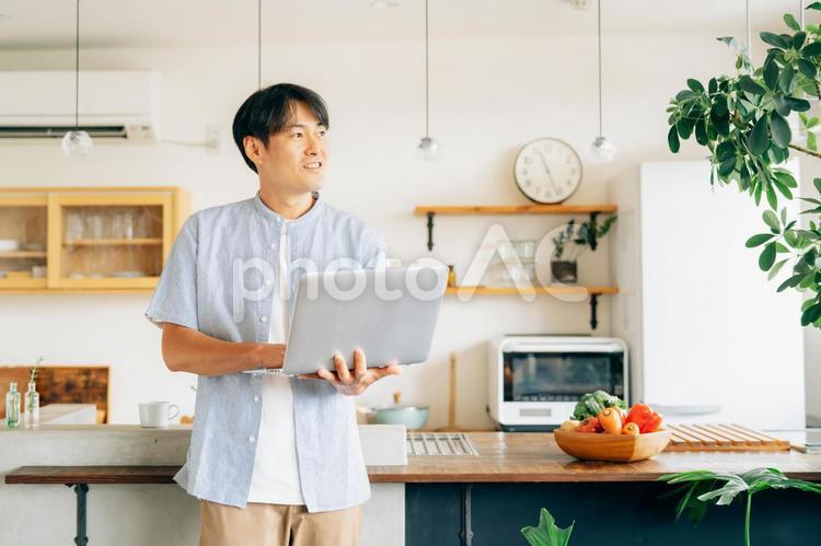 キッチンの前でパソコンを使う男性（笑顔） テレワーク,在宅勤務,パソコンの写真素材
