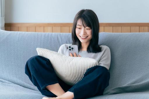 ソファに座ってスマホを使う笑顔の女性 ソファに座ってスマホを使う笑顔の女性の写真