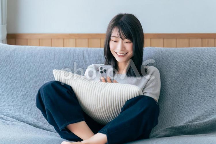 ソファに座ってスマホを使う笑顔の女性 女性,スマホ,スマートフォンの写真素材