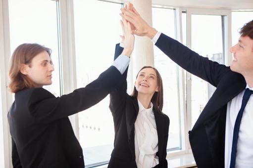 窓際で手を伸ばしハイタッチする外国人3人 男女,外国人,ビジネスの写真素材