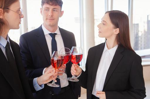 赤い飲み物のグラスを持ち話すスーツの男女の写真