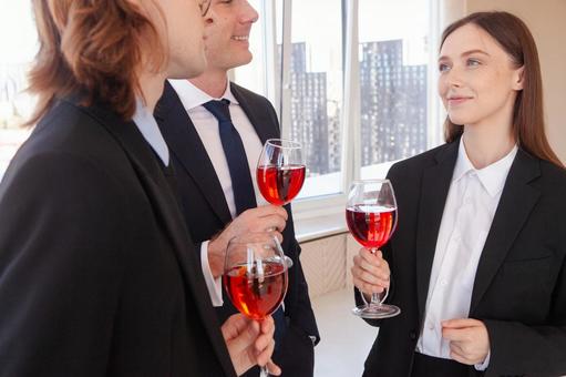 ワイングラスを持ち男性たちの方を見る女性の写真