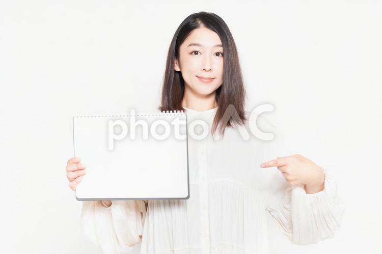 白い背景の前に立って、小さいスケッチブックを見せる主婦 スケッチブック,白紙,主婦の写真素材