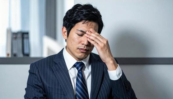 目を手で押さえて苦しむ日本人ビジネスマン 目を手で押さえて苦しむ日本人ビジネスマンの写真