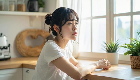 疲れた表情でキッチンに座る若い女性 疲れた表情でキッチンに座る若い女性の写真