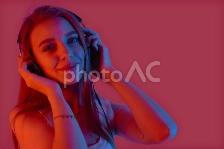 ヘッドフォンを両手で押さえてカメラ目線の女性 女性,マゼンタ,赤の写真素材
