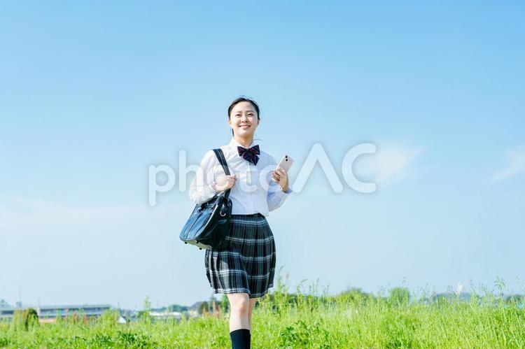 青空の下を歩く女子高校生 スマホ,高校生,笑顔の写真素材