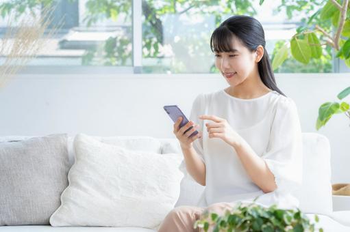 リビングでスマホを見る若い女性 リビングでスマホを見る若い女性の写真