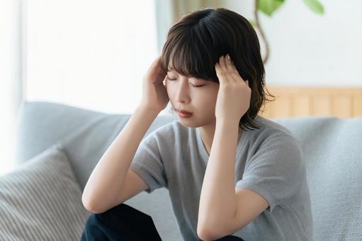 頭を押さえて悩む女性 頭を押さえて悩む女性の写真