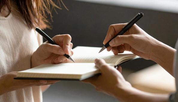 メモ帳を用いて筆談をする若い女性の友人の写真