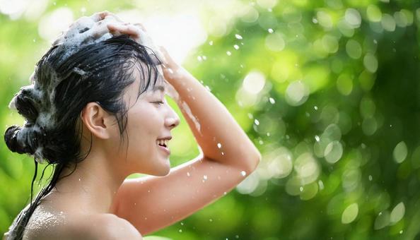 自然の中でシャンプーで髪を洗う女性の写真