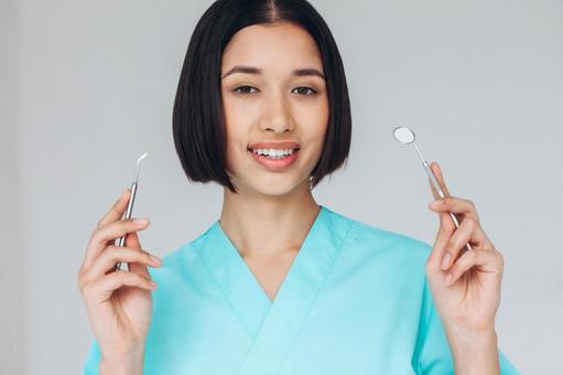 カメラ目線で医療器具と鏡を持っているスクラブの女性 カメラ目線で医療器具と鏡を持っているスクラブの女性 女性,歯科医,鏡の写真素材
