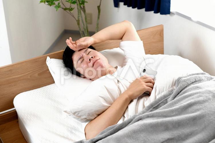 ベッドの上でスマホを持ちながら困る男性 スマホ,ベッド,スマートフォンの写真素材