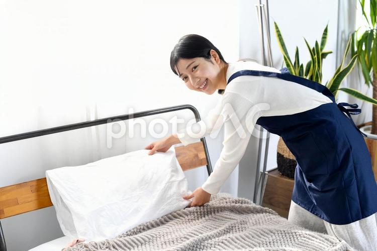 ベッドメイキングをするエプロン姿の女性 ベッドメイキング,ベッド,ベッドメイクの写真素材